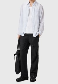 Vaaleansininen nappikauluspaita valkoisen topin kanssa, yhdistetty mustiin cargo-housuihin ja mustiin kenkiin. Mukana olkalaukku.