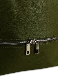 Groene gestructureerde leren oppervlakte met een horizontale zilveren rits met twee rechthoekige trekkers die gedeeltelijk gesloten zijn.