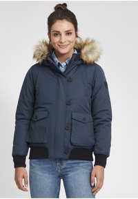 Jūrinės puffer tipo striukės su dirbtiniu kailio gaubtu, turinčios keturis kišenius, mygtukų užsegimą ir raštuotas rankoves. Glotni tekstūra su šiltinimo dizainu.