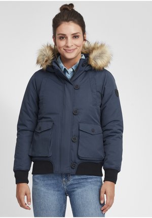 Veste matelassée marine avec capuche en fausse fourrure, dotée de quatre poches, fermeture à boutons et poignets côtelés. Texture lisse avec un design isolé.