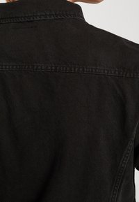 Svart denimjacka med skjortkrage, synliga sömmar och en slät yta. Utsikten visar baksidan och axelområdet.