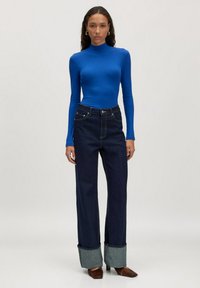 Königsblaues, geripptes Langarmshirt kombiniert mit hoch taillierten, dunklen Jeans aus Denim mit aufgerollten Säumen in einem helleren Denimton.