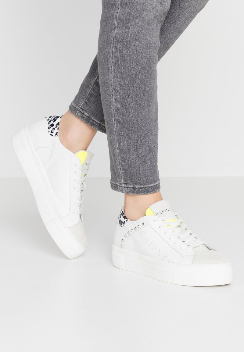 Baskets blanches en cuir avec des accents en textile gris, talon en imprimé léopard et langue en néon jaune. Semelle épaisse blanche avec des clous argentés.