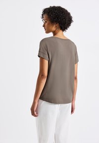 Gray short-sleeve top with rolled cuffs, soft texture, and a relaxed fit; worn with white loose-fitting pants, showcasing a minimalist design.