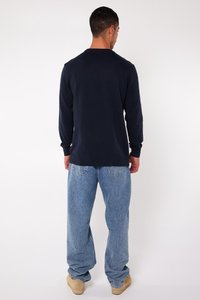 Marineblauer langer Pullover mit Rundhalsausschnitt, kombiniert mit hellblauen, lässigen Jeans und beigen Schuhen. Rückansicht, keine sichtbaren Details.