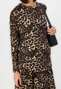 Leopardprint top met lange mouwen in beige en zwart, gemaakt van zachte stof, met een ronde halslijn en een losse pasvorm. Gecombineerd met een zwarte handtas.