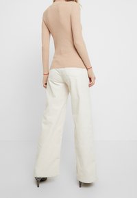 Beige geribbelde langpols top met rode manchetten, gecombineerd met wijde crèmekleurige corduroy broek. De aansluitende vorm accentueert de silhouet.