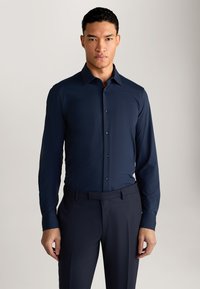 Donkerblauwe blouse met lange mouwen, knoopsluiting en een gespreide kraag, vervaardigd uit soepel stof met een subtiele glans. Combineert goed met donkere, op maat gemaakte broeken.
