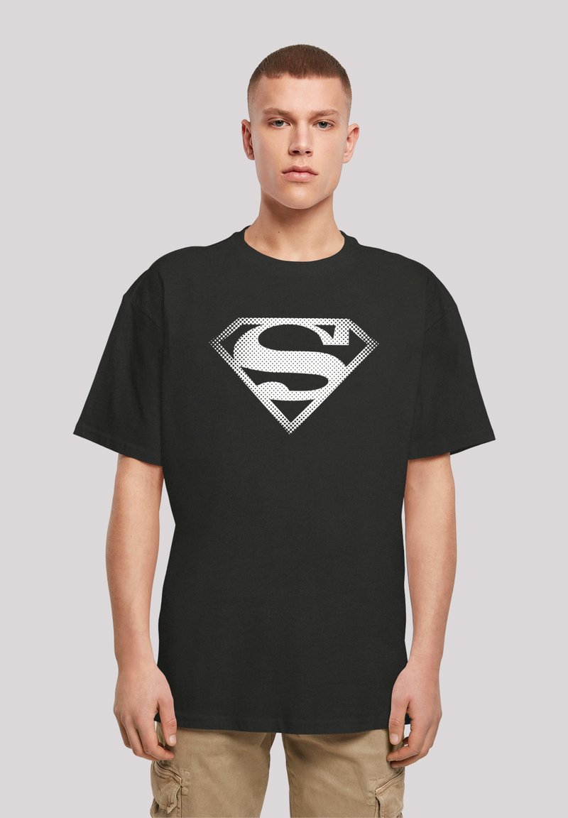Must värviline T-särk mustast puuvillast, millel on suur valge Superman'i logo punktmustriga, ümmargune kaelus ja lõdvestatud istuvus, mudel seismas lihtsa tausta ees.