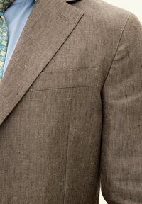 Brauner strukturierter Blazer mit Reverskragen und einer einzigen Brusttasche, kombiniert mit einem hellblauen Hemd und einer gemusterten Krawatte.