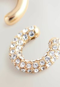 Guldtonede hoop øreringe med et buet design prydet med klare rhinsten i et klynget mønster, der fremhæver en skinnende, tekstureret overflade.