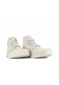 Zapatillas altas de lona beige claro con cordones grises, suela de goma texturizada y detalles del logo en la lengüeta.