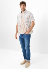 Camicetta a maniche corte a quadri nei colori pastello, jeans in denim e scarpe slip-on beige. La camicia presenta un design con bottoni e una vestibilità comoda.
