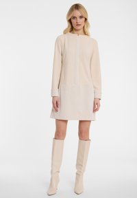 Beiges Kleid mit langen Ärmeln und rundem Ausschnitt, mit einem gerippten Stoff am Saum und an den Bündchen, kombiniert mit knielangen beigen Stiefeln.