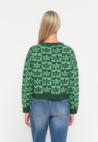 Green knitted sweater with a cropped design featuring a floral pattern in varying shades of green. Ribbed hem and cuffs.