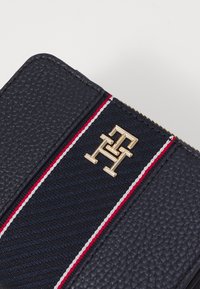 Navy leather wallet featuring a textured surface, gold logo, and a vertical stripe pattern with red and white accents. Zipper closure.