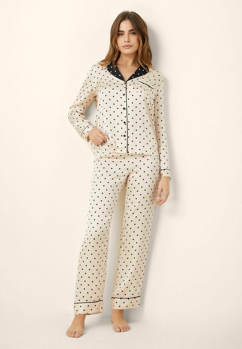 Polka dot pajama set in cream satin with black accents. Long-sleeve shirt features a notch collar; pants have an elastic waistband.