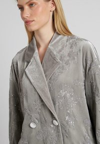 Blazer de terciopelo gris con bordados florales y lentejuelas, diseño de doble botonadura, amplios solapas de muesca y botones redondos.