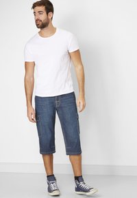 White cotton t-shirt, blue denim cargo shorts with multiple pockets, above-the-knee length, worn with blue canvas sneakers.