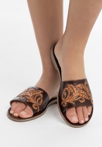 Bruine leren slippers met geambosserde bloempatronen, open teen ontwerp, gevoerde binnenzool en platte zool.