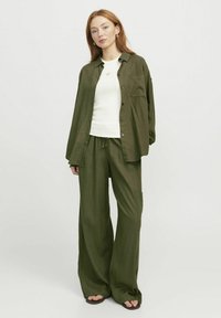 Tenue vert olive comprenant une chemise à boutons ample et un pantalon large en tissu texturé. Haut ajusté blanc en dessous, au design minimaliste.