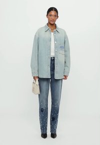 Lichtblauwe oversized denimjas met een patch pocket. Gecombineerd met donkerblauwe denimjeans met witte verfspetters en vredessymbolen. Zwarte hakken.