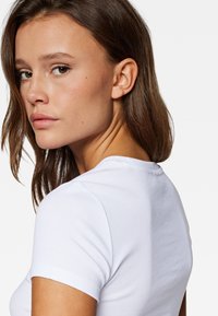 White cotton t-shirt with short sleeves and a crew neckline, featuring a smooth texture and fitted design. Positioned against a white background.