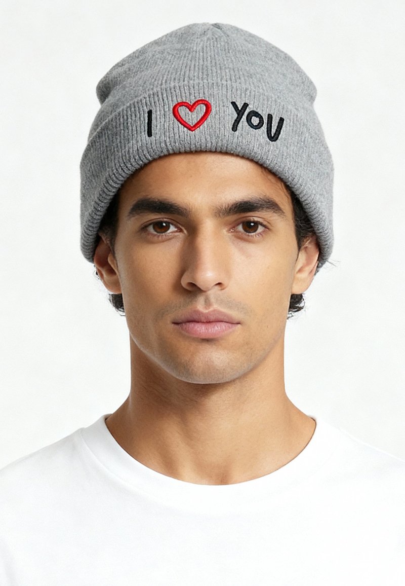 Grijze gebreide muts met geribbelde textuur, met een rood hart en zwarte tekst "I ♥ YOU" geborduurd aan de voorkant. Eronder een effen wit T-shirt.