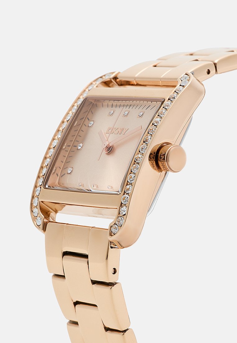 Reloj de metal color oro rosa con una caja rectangular, esfera en tono blush texturizada y acentos de piedras brillantes en el bisel. Los eslabones son suaves y pulidos.