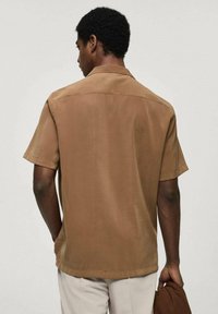 Korte mouwen, gekraagde blouse van effen bruine stof. Kenmerkt zich door een relaxte pasvorm en een gladde textuur, zonder zichtbare patronen of versieringen.