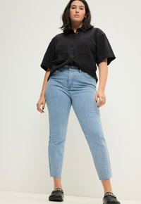 Camisa negra de manga corta con botones, jeans de tiro alto a rayas en azul claro y zapatos negros sin cordones. Diseño sencillo y texturas suaves.