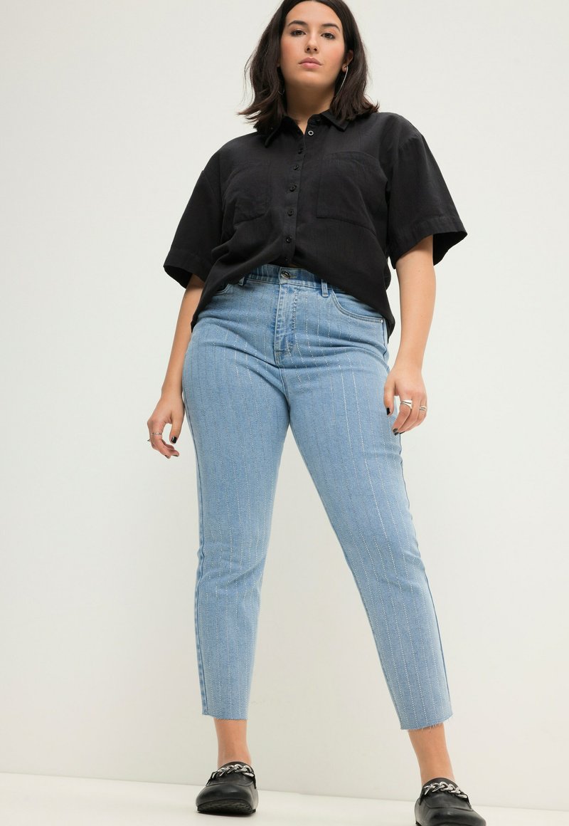 Camisa negra de manga corta con botones, jeans de tiro alto a rayas en azul claro y zapatos negros sin cordones. Diseño sencillo y texturas suaves.