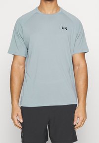 Ljusblå atletisk t-shirt med korta ärmar, rundad hals och svart logotyp på bröstet. Mjuk, ventilerande tyg med en slät struktur.