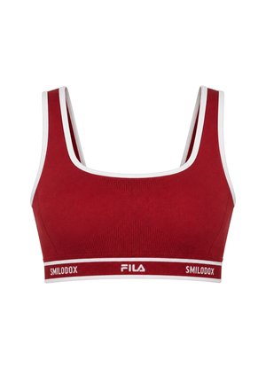 Mujer de pie mirando hacia adelante, lleva un top corto deportivo rojo a juego y mallas con logotipos en blanco y negro, y zapatillas blancas.