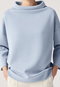 Felpa azzurra con colletto cowl, maniche tre quarti e una superficie morbida e liscia. Presenta una vestibilità comoda e dettagli di cucitura minimi.