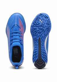 Blaue Sportschuhe mit einer strukturierten Oberseite, die rote Akzente und weiße Streifen aufweist. Die Sohle hat ein geformtes Design für besseren Halt.