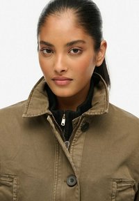 Bruine jacket met een ritskraag en zwarte gebreide binnenvoering, met een enkele knoopsluiting en zijzakken. Glad van textuur.