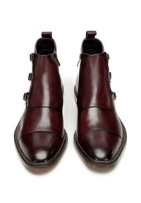 Botas de cuero burdeos hasta el tobillo con acabado pulido, que cuentan con tres hebillas metálicas, punta redondeada y una pequeña lengüeta en la parte trasera.