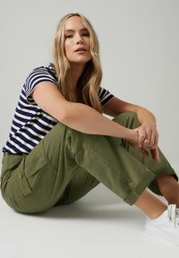 Gestreepte marineblauwe en witte t-shirt gecombineerd met olijfgroene cargobroek met zijzakken en omgeslagen broekspijpen. Draag met witte sneakers.