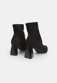 Des bottines noires en suède présentent un talon carré et une fermeture par zip sur le côté. Le design est élégant avec une texture lisse et une forme ajustée.