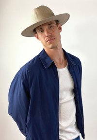 Marineblaue Jacke, weißes T-Shirt, Strohhut mit breiter Krempe. Lässiger Schnitt, glatte Textur, taillierter Kragen und Reißverschluss vorne.