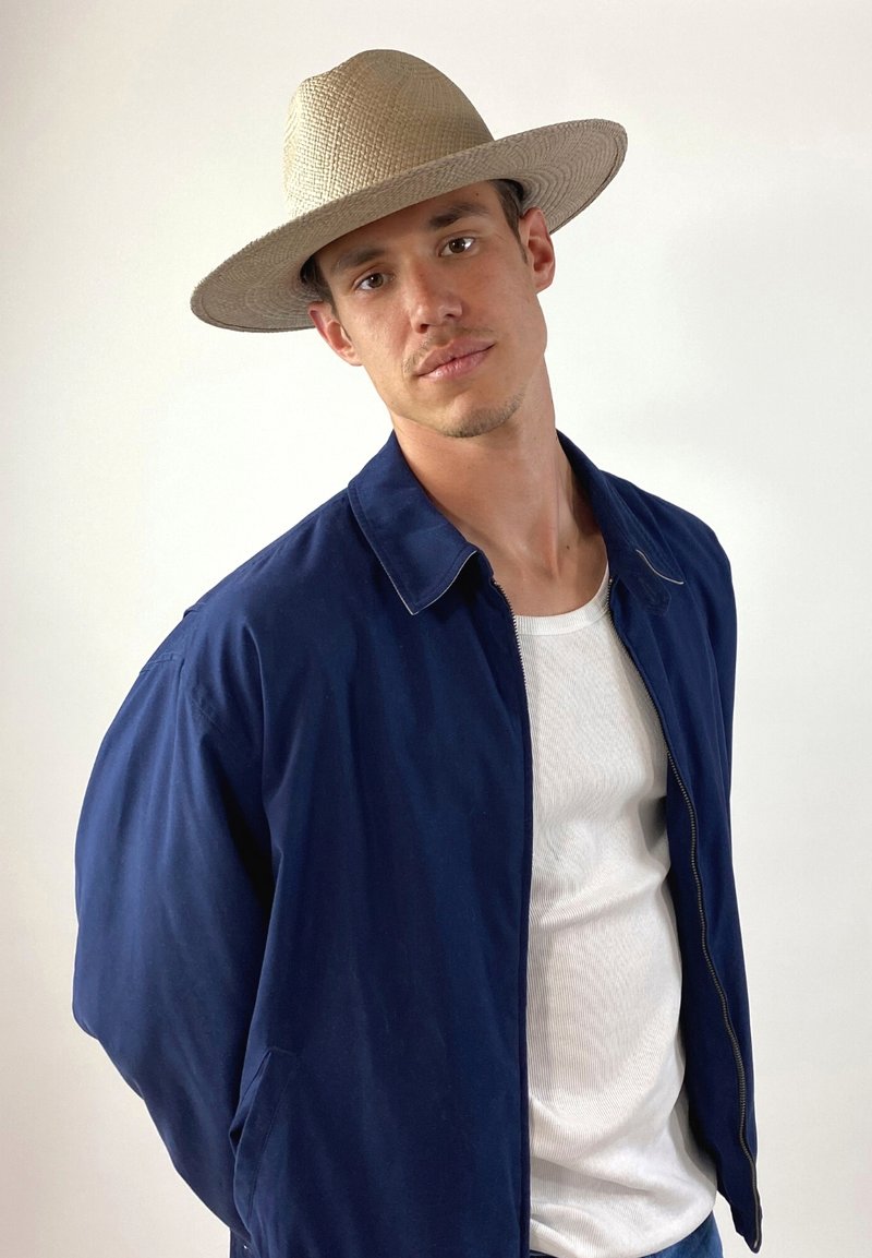 Marineblaue Jacke, weißes T-Shirt, Strohhut mit breiter Krempe. Lässiger Schnitt, glatte Textur, taillierter Kragen und Reißverschluss vorne.