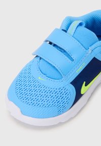 Chaussure de sport bleue avec tige en mesh, semelle flexible et bandes Velcro. Présente un accent marine et un petit détail de logo jaune.
