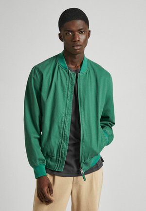 Veste bomber verte en tissu léger et texturé avec col et poignets côtelés, présentant une fermeture éclair et des poches latérales.