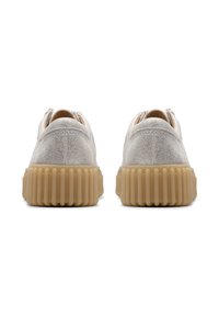 Ein Paar hellgraue Wildledersneaker mit dicken, gerippten beigefarbenen Gummisohlen, von hinten auf einem weißen Hintergrund betrachtet.