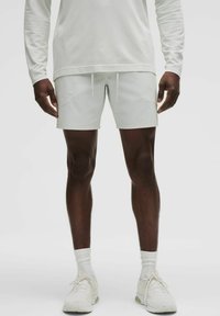Weißes Langarmoberteil mit strukturiertem Design, kombiniert mit hellen Shorts mit elastischem Bund und Kordelzügen; schlichtes Design.