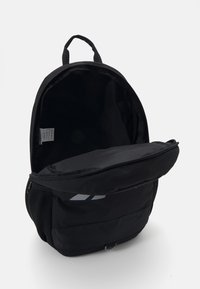 Svart ryggsekk med glidelås i hovedrommet, polstret bak og nettlommer på sidene. Har et elegant design og minimale merkevareakkenter.