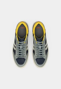 Σκούρα μπλε και γκρι δερμάτινα αθλητικά παπούτσια με κίτρινα διακοσμητικά, στρογγυλή μύτη, σχέδιο με κορδόνια, με υφασμένο πάτο και λογότυπο της μάρκας στη γλώσσα.