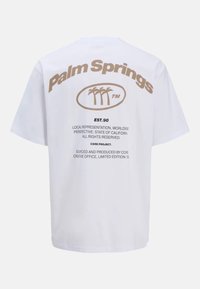 T-shirt en coton blanc avec le texte "Palm Springs" en marron clair, un graphique de palmier et d'autres détails imprimés au dos.