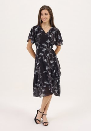 Robe portefeuille noire à imprimé floral, avec des manches courtes flottantes, une jupe superposée et un motif floral blanc. Tissu léger avec une texture fluide.
